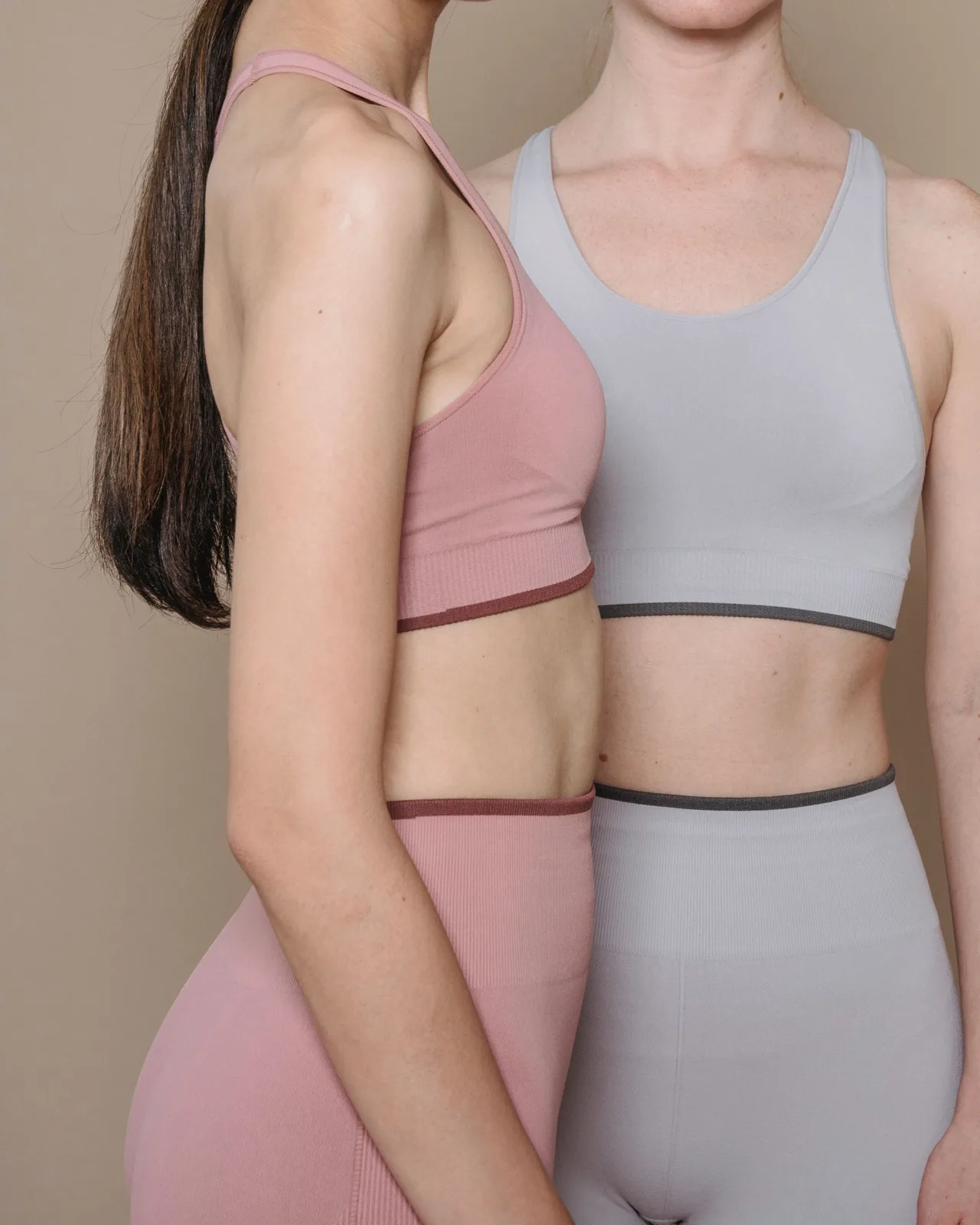 Two women wearing the same seamless sports bra and leggings set in pink and grey
