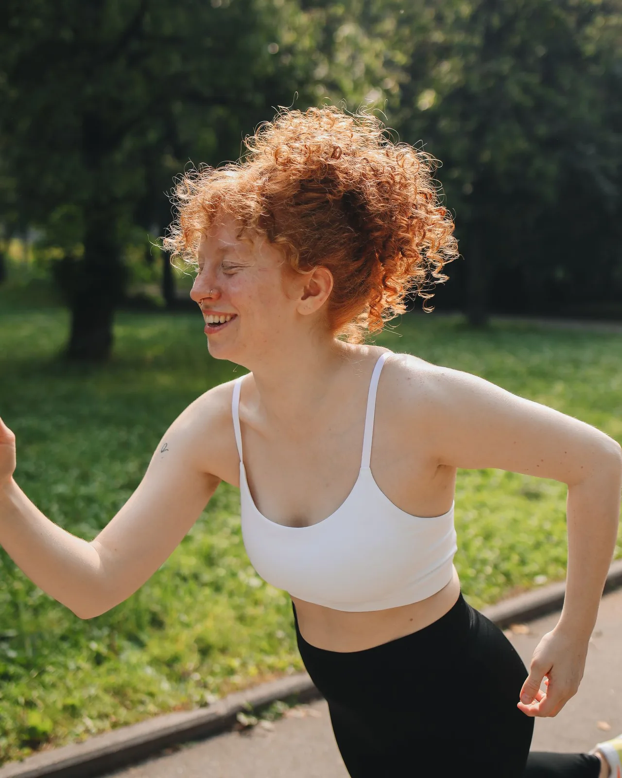 Woman running in a park wearing a white scoop neck sports bra with thin straps and black leggings