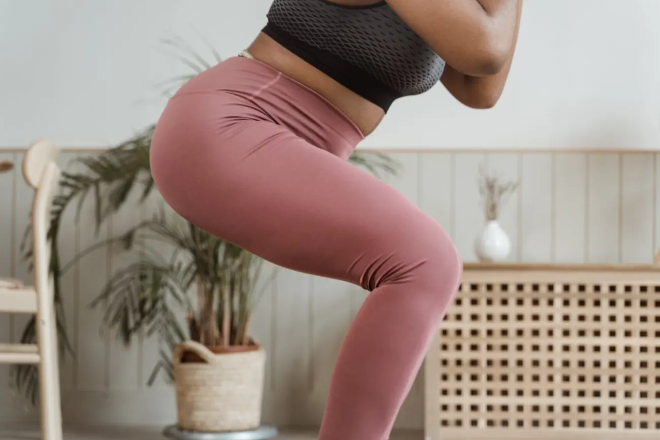Close-up of a woman in pink leggings in a deep squat, showing the fabric stretched across the seat and thighs